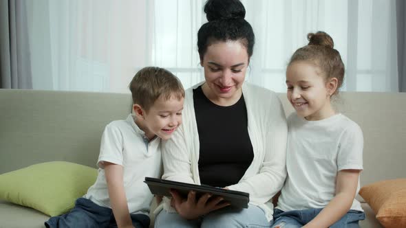Happy Mom with Children Sitting on the Couch and Watching the Tablet Mom is Playing with the alt