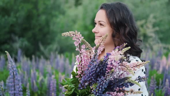 Young Beautiful Woman Posing in a Field with a Bouquet of Lilac Flowers. Happy Brunette in a Field alt