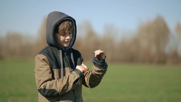 The Boy Holds a Fishing Line in His Hands and Launches a Multicolored Kite alt
