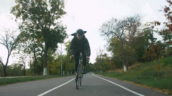 Young Hipster Man in Helmet Riding Fixed Gear Bicycle in Park During Autumn Morning alt