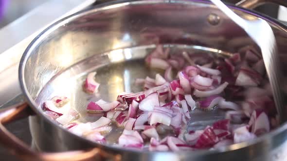 The chef mixes the onions in a saucepan. Steam rises from the pan