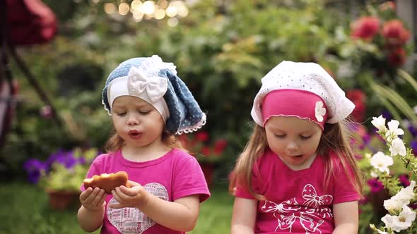 Adorable Little Girls in Summer Hats Eating Delicious Cookies in the Garden alt