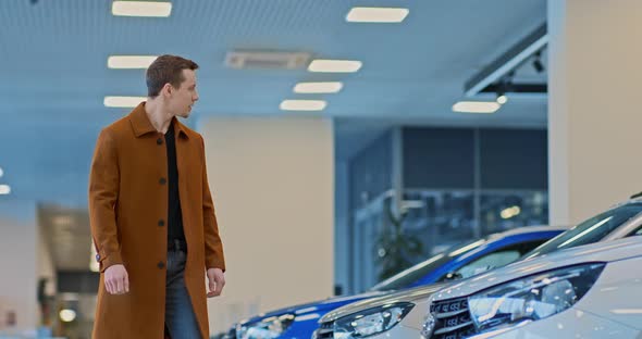 Young Male Businessman Walks Through a Car Dealership and Looks at New Models of Cars