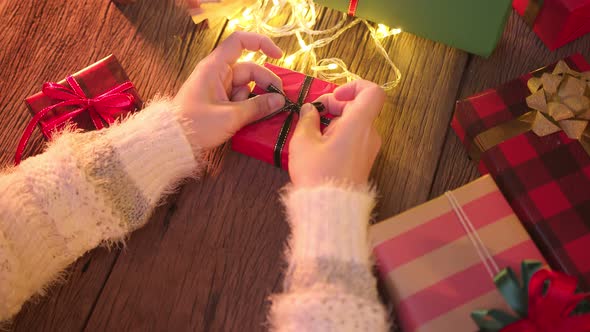 close-up asian female hand tying a bow ribbon on a box with a gift on a wooden table alt