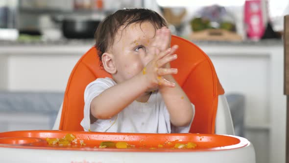 Funny Kid Sits in a Chair for Feeding Children and Claps His Hands Eats Himself Got Dirty All Over