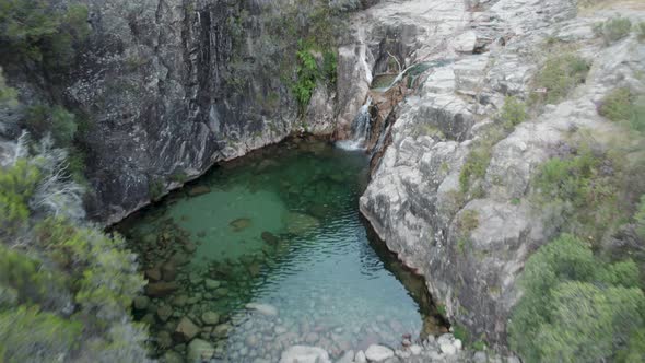 Aerial pullback Over emerald natural pool from waterfall, Gerês National park, Portugal