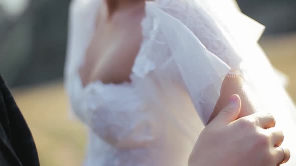 Young Bearded Groom Strokes His Bride By the Hand on the Nature, Focusing on the Girl, Close View alt