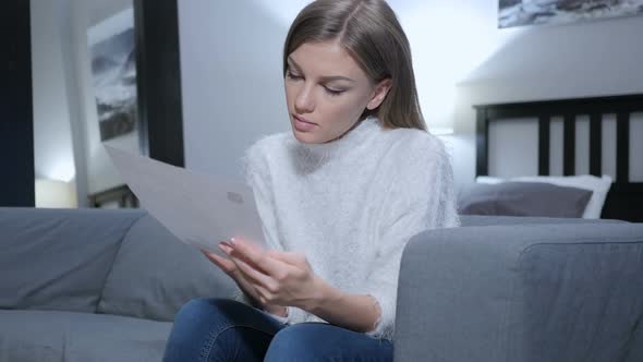 Young Woman Reading Letter while Sitting on Sofa alt