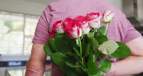 Caucasian senior man giving a flower bouquet to his wife at home alt