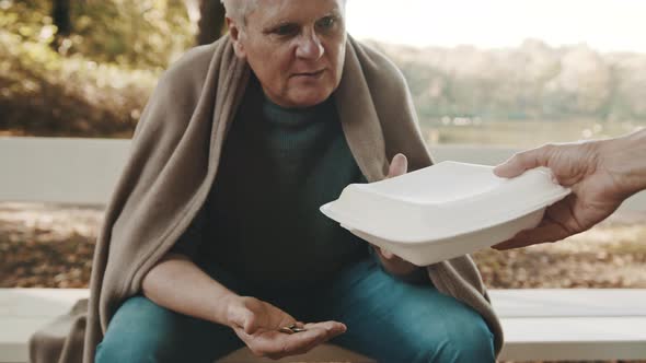 Poor Elderly Homeless Man Counting Left Coins in the Park and Receiving Charity Meal  alt