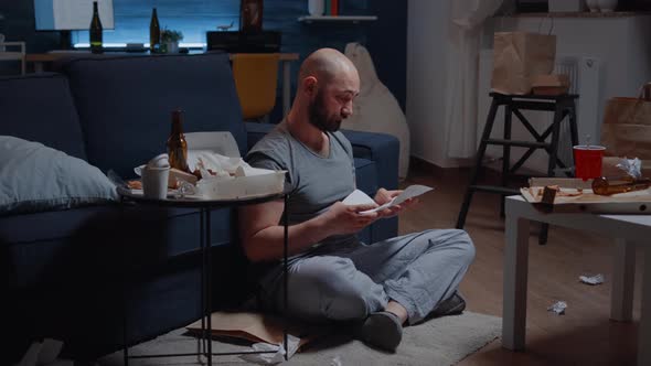 Desperate Adult Man Sitting on Floor Reading with Tears Eviction Notice alt