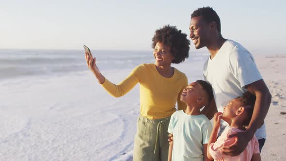Smiling african american family taking selfie and embracing on sunny beach alt