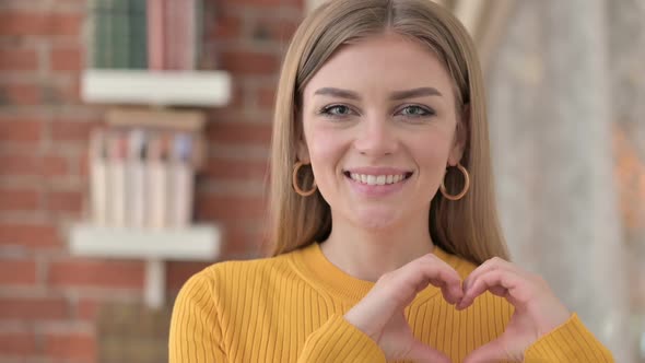 Portrait of Cheerful Young Woman Making Heart Shape with Hand alt
