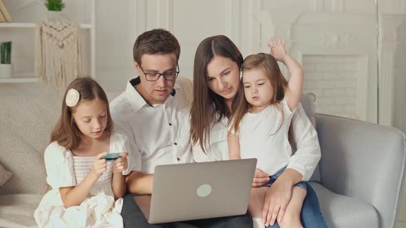 A Happy Family Uses a Laptop for Online Shopping, Sitting on the Couch at Home alt