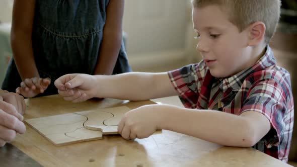 Young girl and boy in wood shop with older man finishing a wood puzzle. alt