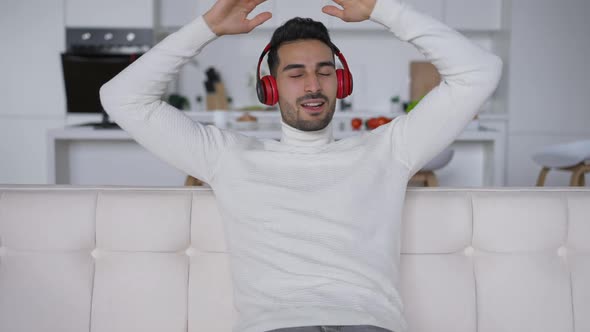 Carefree Relaxed Handsome Middle Eastern Man Enjoying Music in Headphones Singing Smiling Sitting on alt