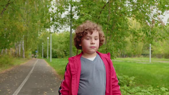 Young Curly Boy Walking on Road in Summer Park alt