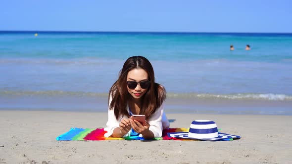 Young asian woman traveler using her smartphone at tropical sand beach