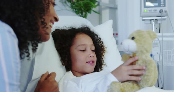 Close-up of African american mother and son playing with teddy bear in the ward at hospital 4k alt