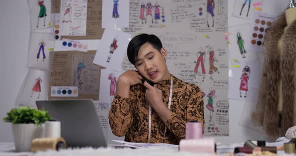 Angry Asian clothing designer talking on mobile in his office alt