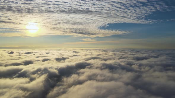 Aerial view of vibrant yellow sunrise over white dense clouds with blue sky overhead. alt