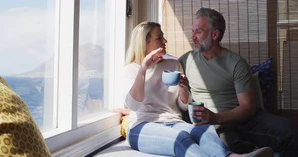 Relaxing caucasian mature couple drinking coffee and talking in sunny living room alt