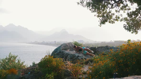 Young Woman Doing Fitness Exercises on Open Air  Leaning on the Rocks and Does Push Ups alt