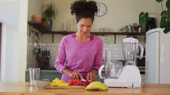 Mixed race woman chopping fruits to make fruit juice in the kitchen at home alt