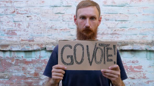 Man shows cardboard with Go Vote sign on brick wall urban background Voting concept Use your voice