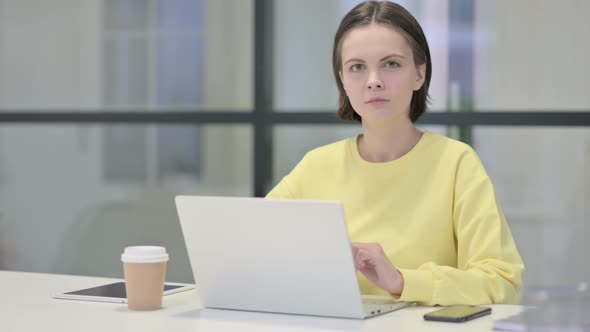 Young Woman Looking at Camera While Using Laptop in Office alt
