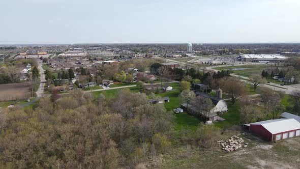 Panoramic view of edge of community with diverse buildings and roads, water tower and hazy sky.