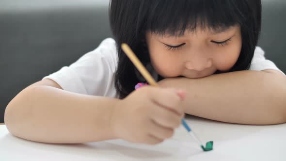 Close up happy Asian girl drawing picture with water color on paper. alt