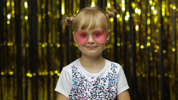 Child Show Ok Sign, Smiling, Looking at Camera. Girl Posing on Background with Foil Golden Curtain alt