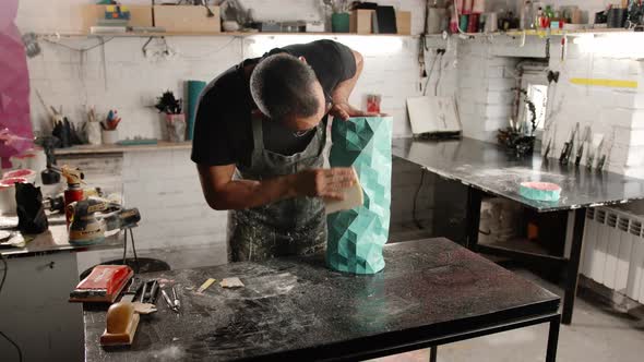 Male artisan artist sculptor wipes the product, puts things in order in the workshop alt