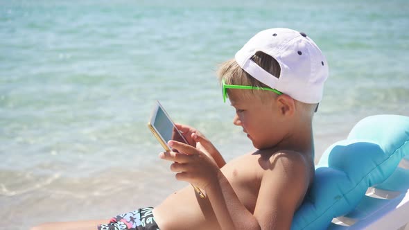 Funny Child Uses a Tablet on the Beach