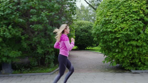 Fit Girl Runs Along City Park alt