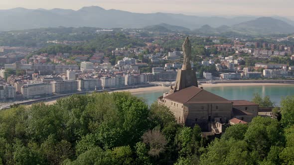 Monument statue with city of San Sebastian in background, cinematic aerial drone view alt
