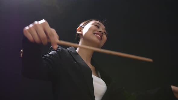 Asian Conductor Woman Holding A Baton Closing Her Eyes And Showing Gesture In The Black Studio alt