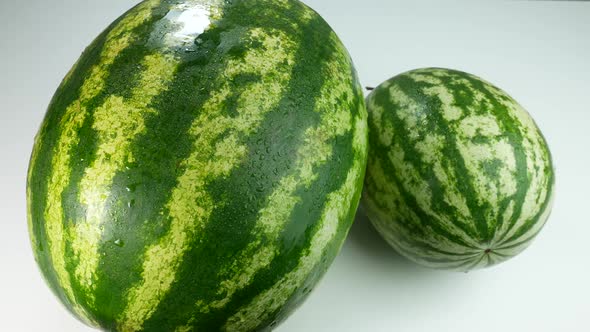 Two Watermelons On A White Surface Covered In Drops Of Water