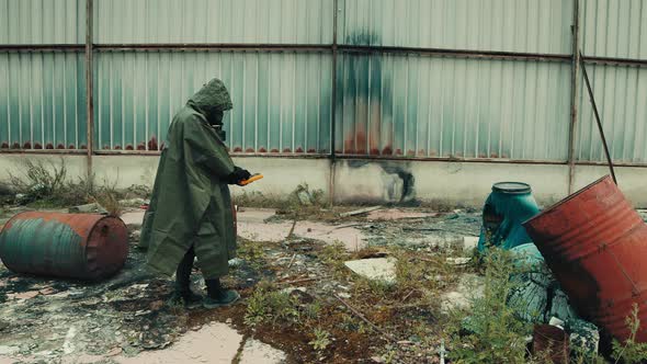 Man with Gas Mask Checks the Radiation Level with the Geiger Counter in a Shed alt