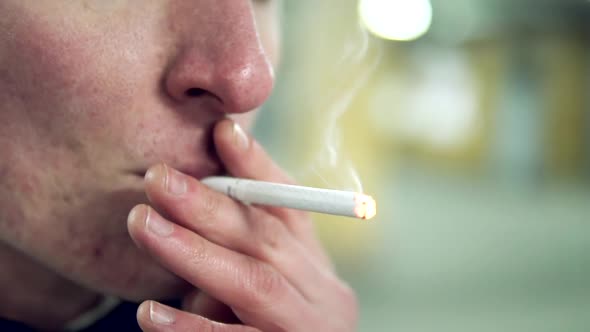 Closeup View of Young Blonde Man in a Black Suit with a Bowtie Smoking a Cigarette in the Parking alt