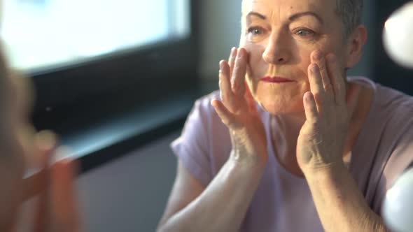 Old Woman Applying Rejuvenating Mask on Her Face Skin alt