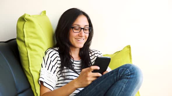 Woman relaxing and using mobile phone on the sofa at home
