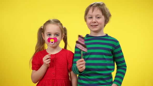 Cheerful Funny Little Girl with Baby's Dummy on Stick and Laughing Cute Boy with Printed Cake Posing alt