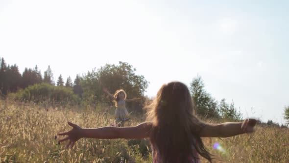 Two little girs running through summer field and embracing each other