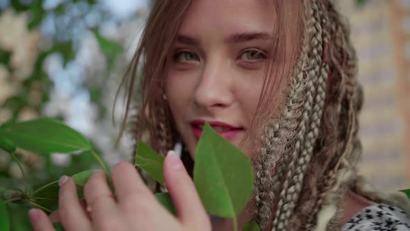 A Cute Girl with Dreadlocks Poses By a Tree with Leaves