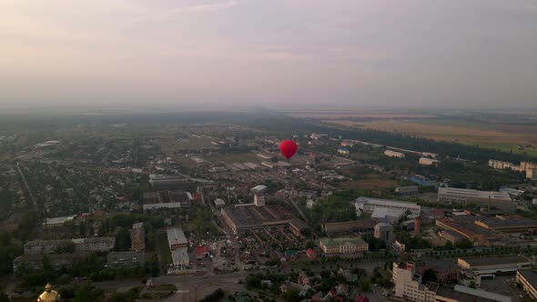 Red Hot Air Balloon Flying Over Buildings in Industrial Zone in Small European City at Summer Sunset alt