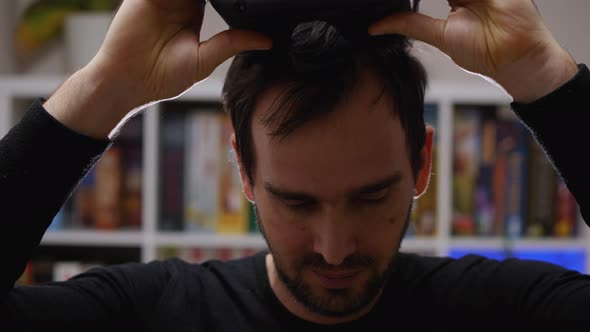Close-up of a bearded man taking VR glasses off his head. Home interior. VR helmet for entertainment alt