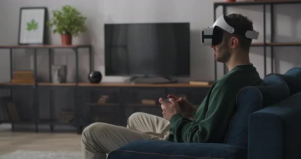 Adult Man Is Playing Modern Computer Game Using Headmounted Display and Joystick Virtual Reality alt