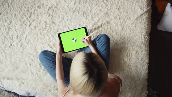 Woman Artist Draws on Graphic Tablet with Chromakey Screen Using Stylus While Sitting on Blanket in alt